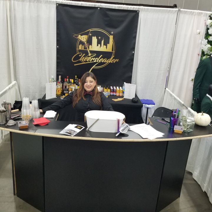 Woman seated at a booth with a black banner, brochures, and bottles displayed at an event table