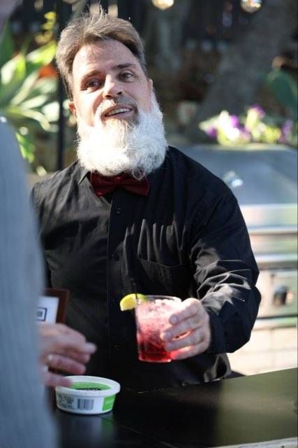 Man in a black shirt holding a red drink with a lemon wedge at an outdoor table