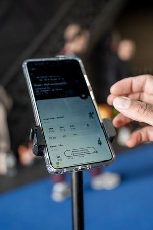 Hand die een smartphone op een standaard vasthoudt en een app-scherm toont tijdens een evenement op de blauwe vloer.