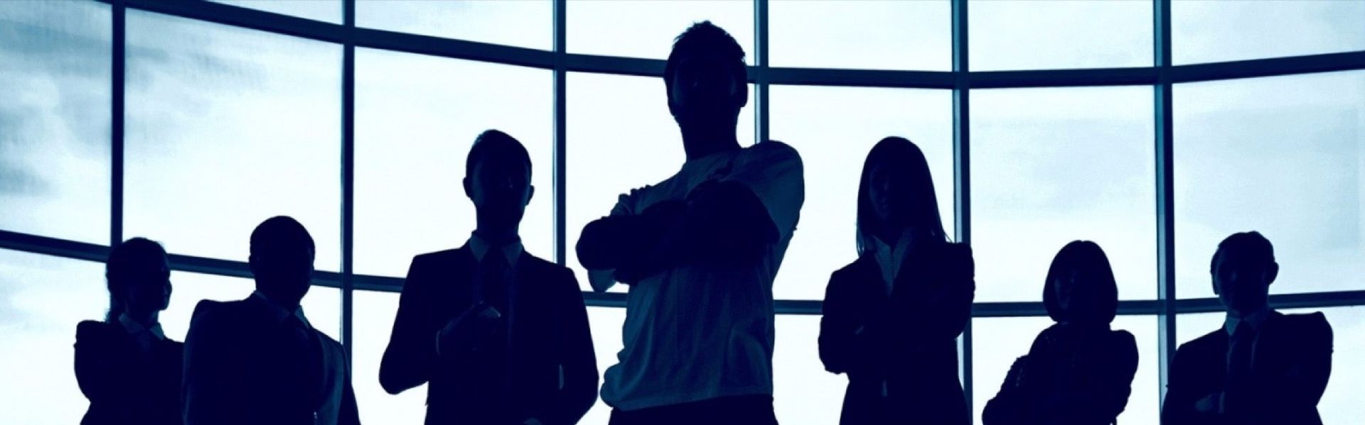 Silhouetted business team in front of a window. One person has arms crossed.