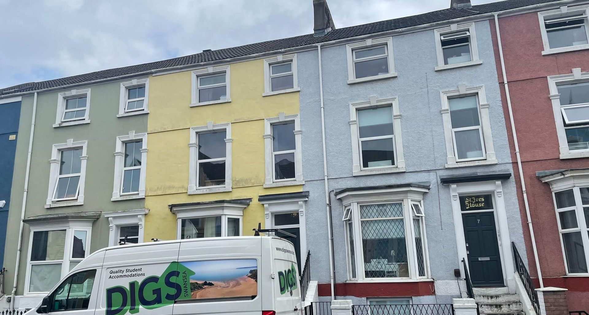 Row of colorful houses: green, yellow, blue, and red. White van with 