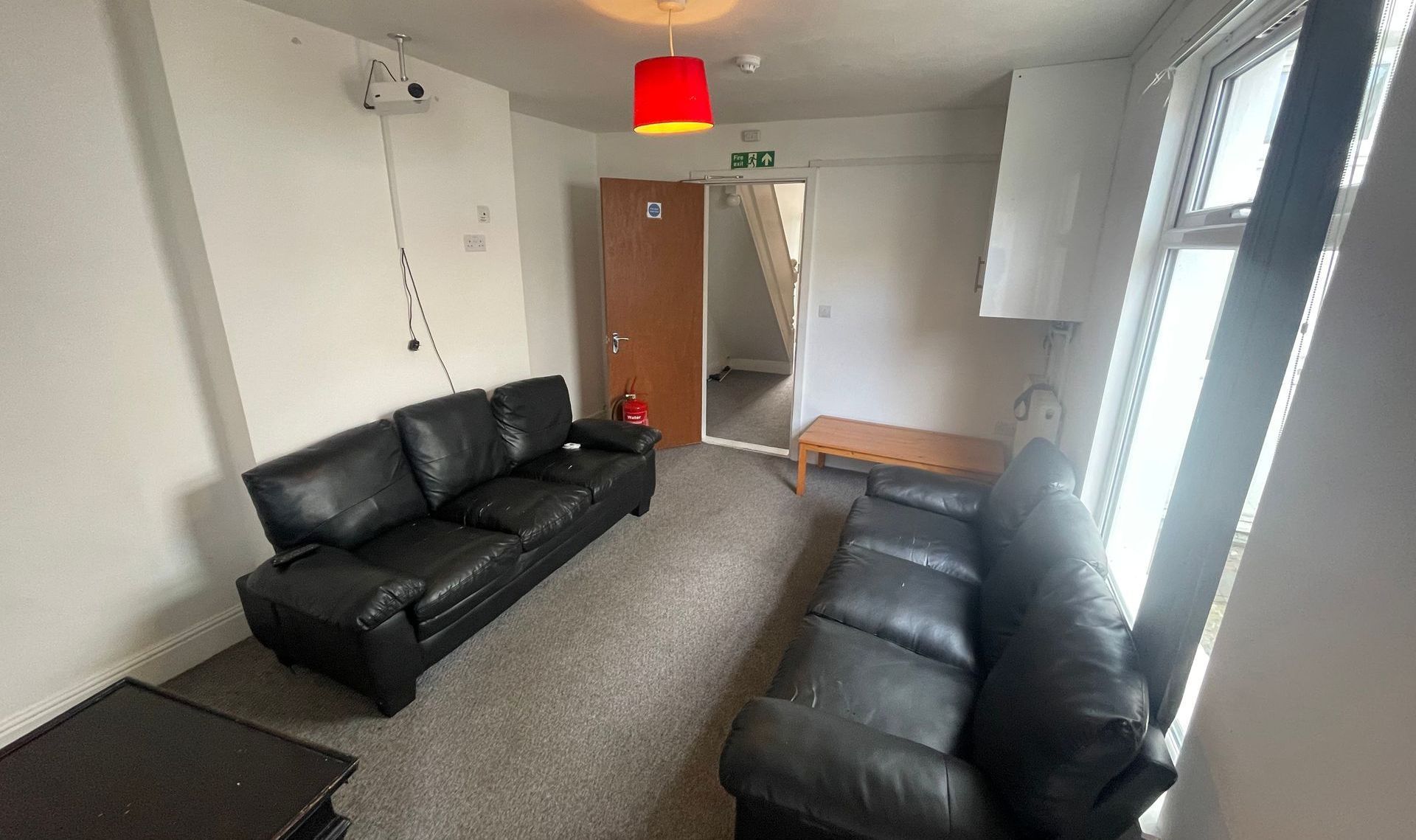 A living room with two black leather couches, a coffee table, and a door leading to a staircase.