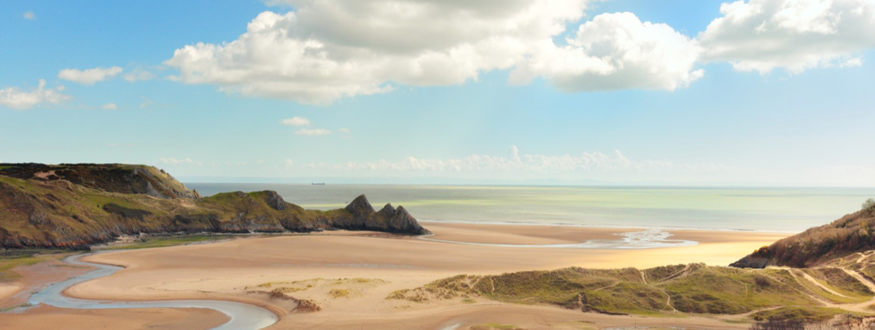 Sandy beach, ocean and coastline. Brown cliffs and sandy dunes. Sunny day with blue sky and white clouds.