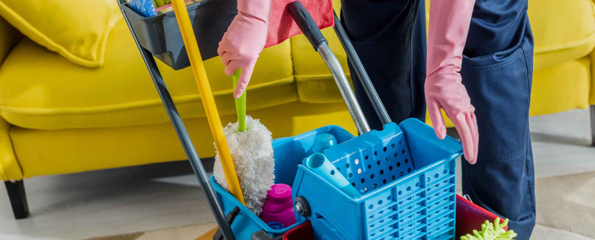 Person in pink gloves using a cleaning cart with yellow couch in background.