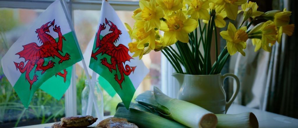Welsh flags, daffodils, leeks, and scones arranged on a windowsill, celebrating St. David's Day.