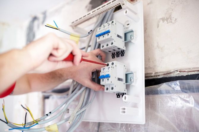 Hand wiring electrical breaker panel with red screwdriver in a wall-mounted box