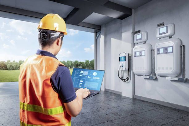 Technician in hard hat using a tablet beside solar inverters and wall-mounted power units indoors