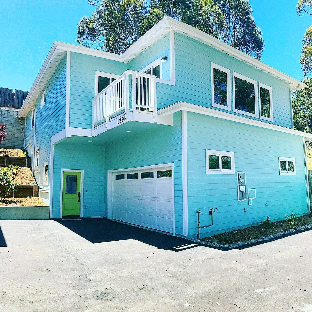 Two-story turquoise house with white trim, a green front door, and a white garage door, set in a sunny environment.