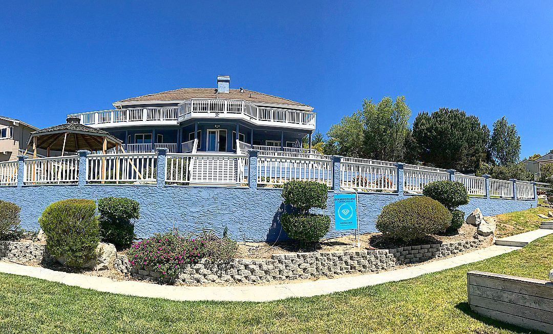 Blue mansion with multiple balconies and white railings, against a blue wall and bright blue sky.