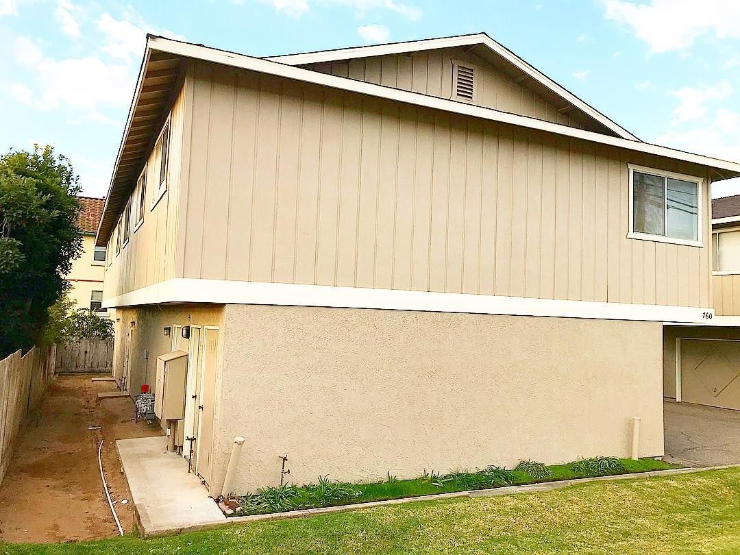 Two-story house with open garage door and balcony, on a concrete lot, with a light brown exterior.