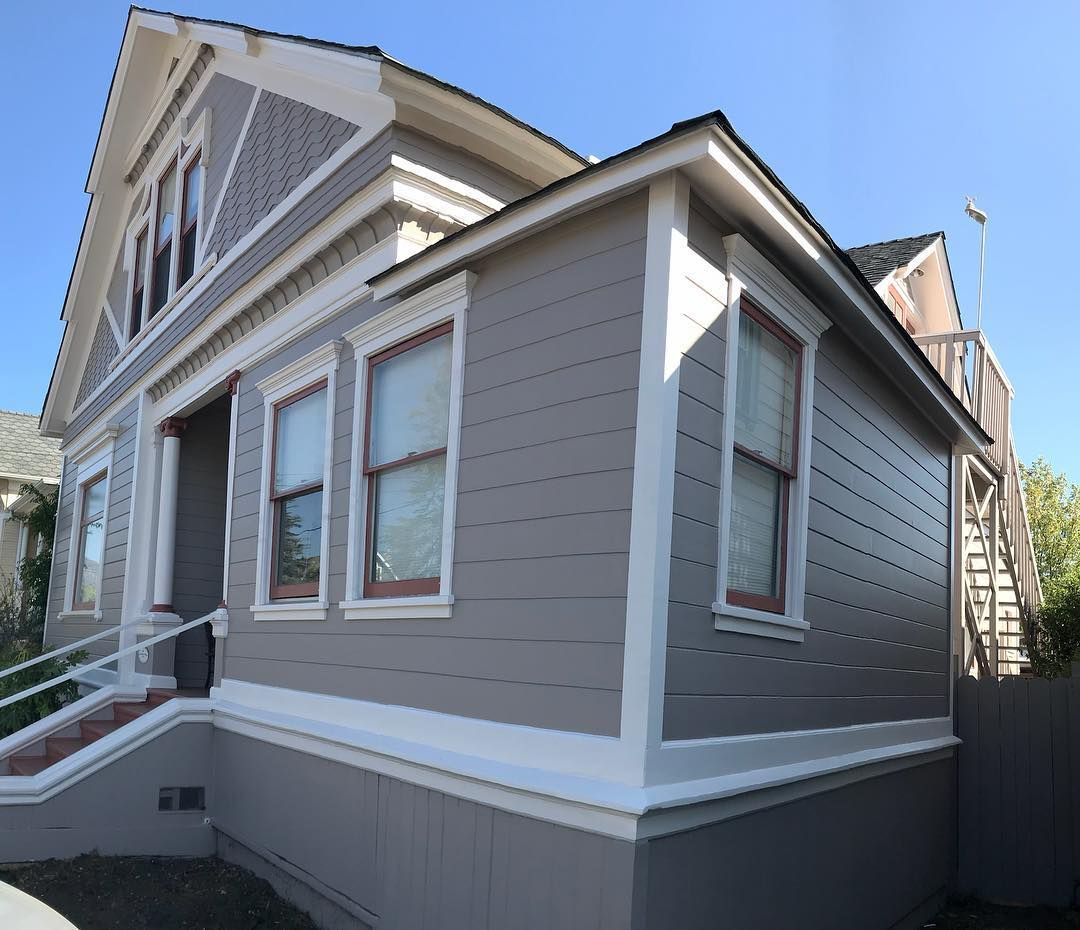 Gray Victorian house with white trim, three windows visible, blue sky.
