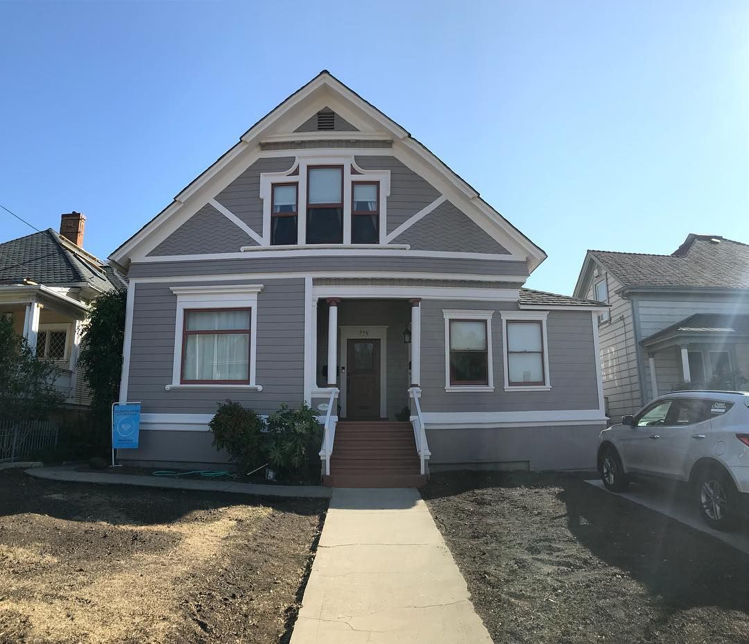 Gray two-story house with front porch, windows, and angled roof, sidewalk leading to the front door.