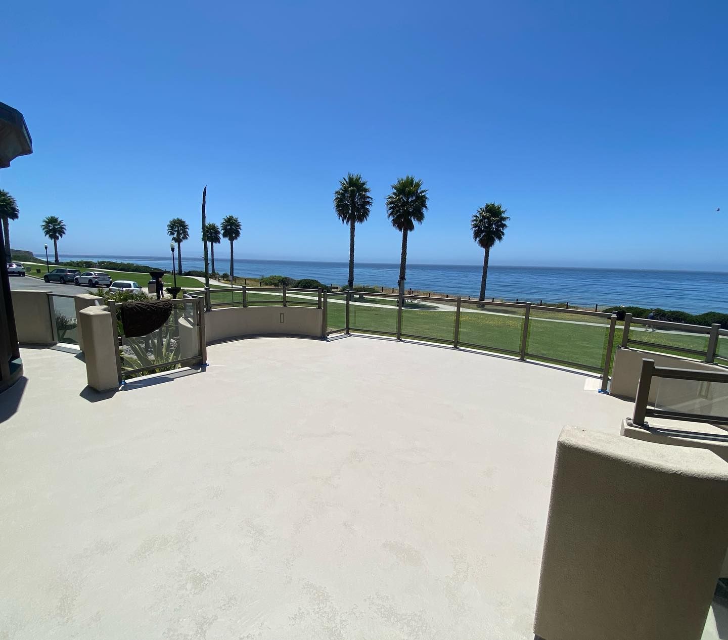 A coastal patio with ocean view, blue sky, palm trees, and tan concrete.