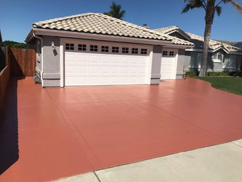 Red painted concrete driveway leading to a house with a white garage door.