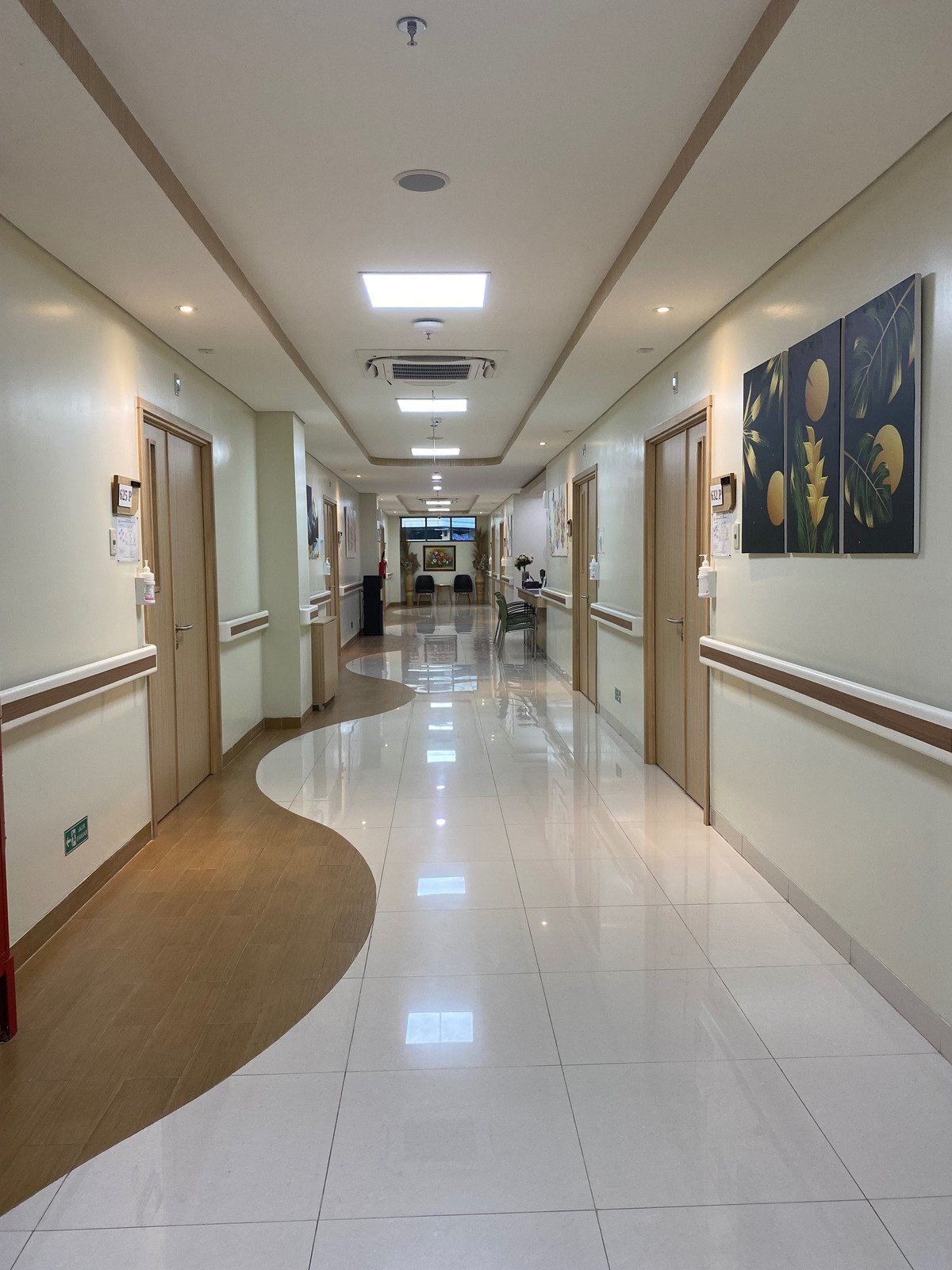 Hospital hallway with tan doors and walls, a patterned floor, and artwork.