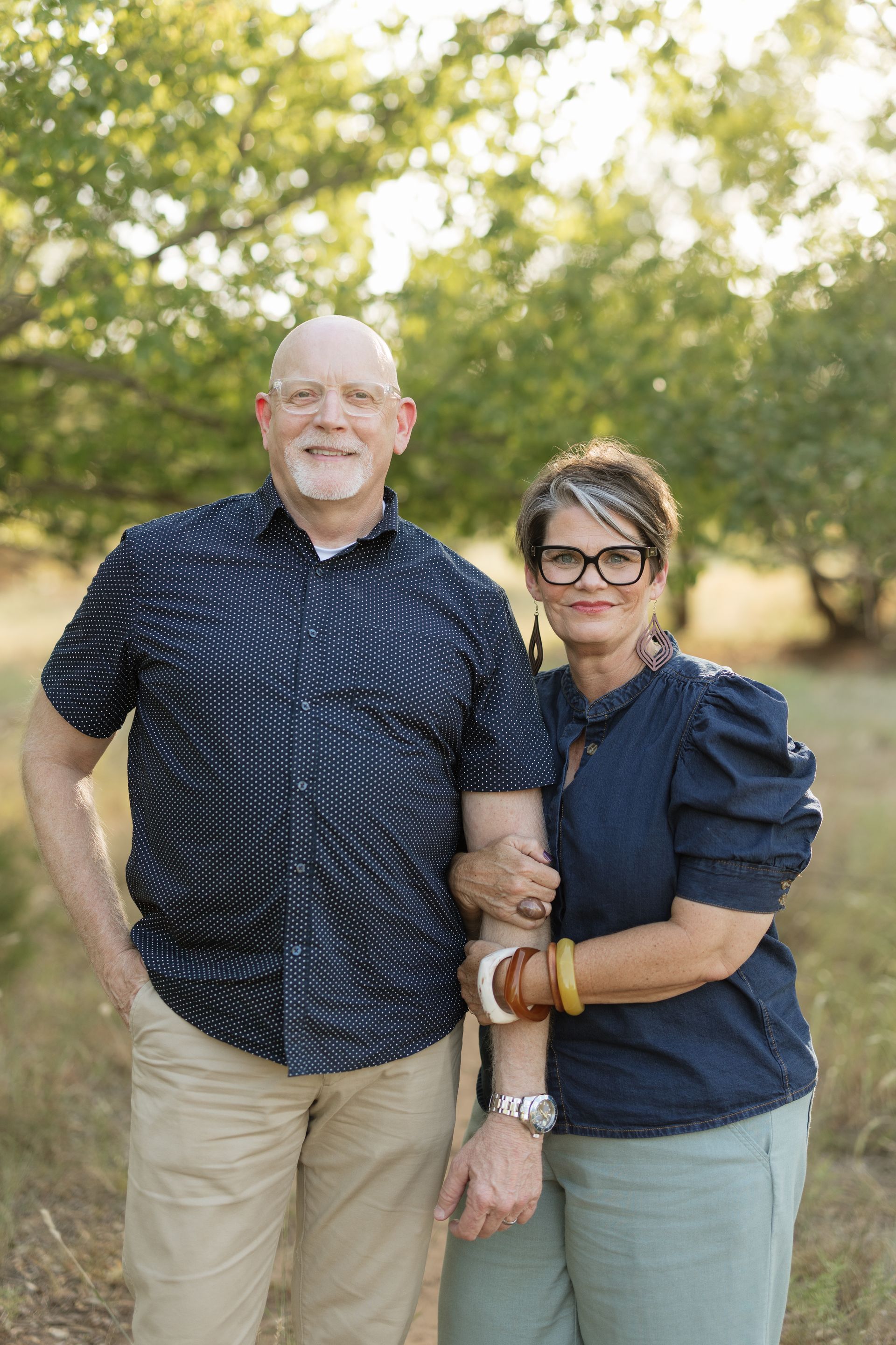 Two people standing against a white wall, smiling and posing casually outdoors.