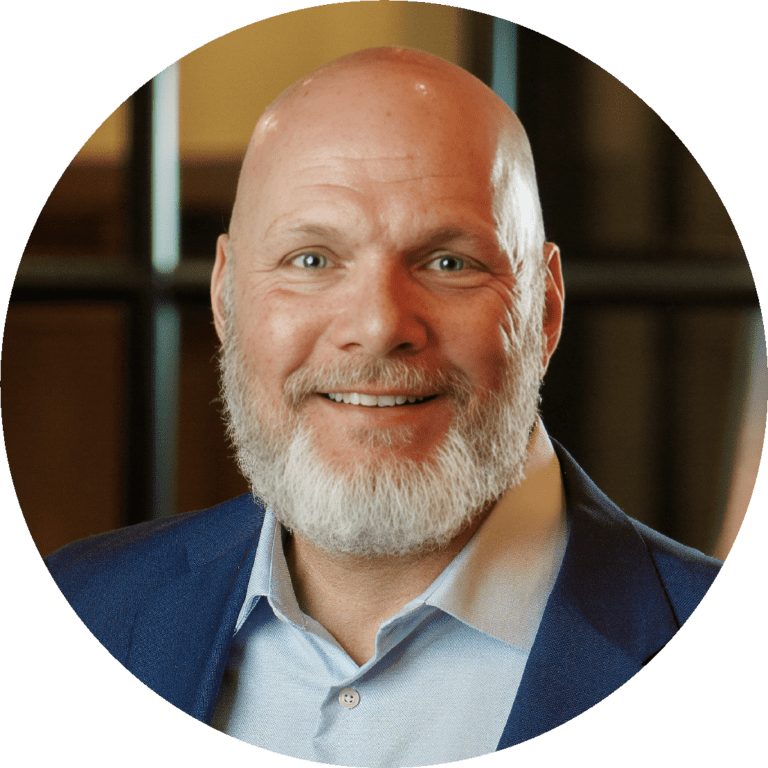 Smiling bald man with a white beard in a blue blazer and light blue shirt, indoors