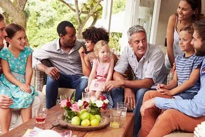 Group of people seated on a patio, chatting around a table with fruit and drinks.