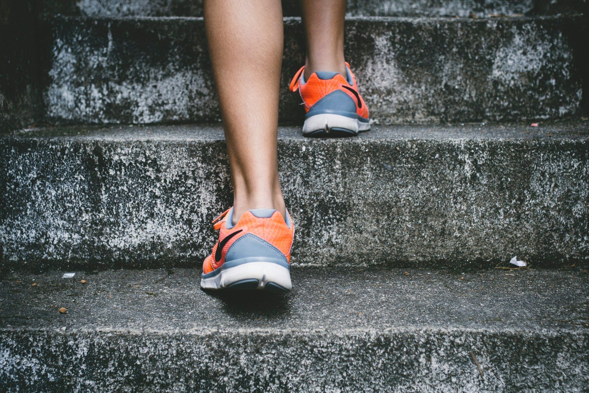 Person walking up weathered concrete steps in orange running shoes