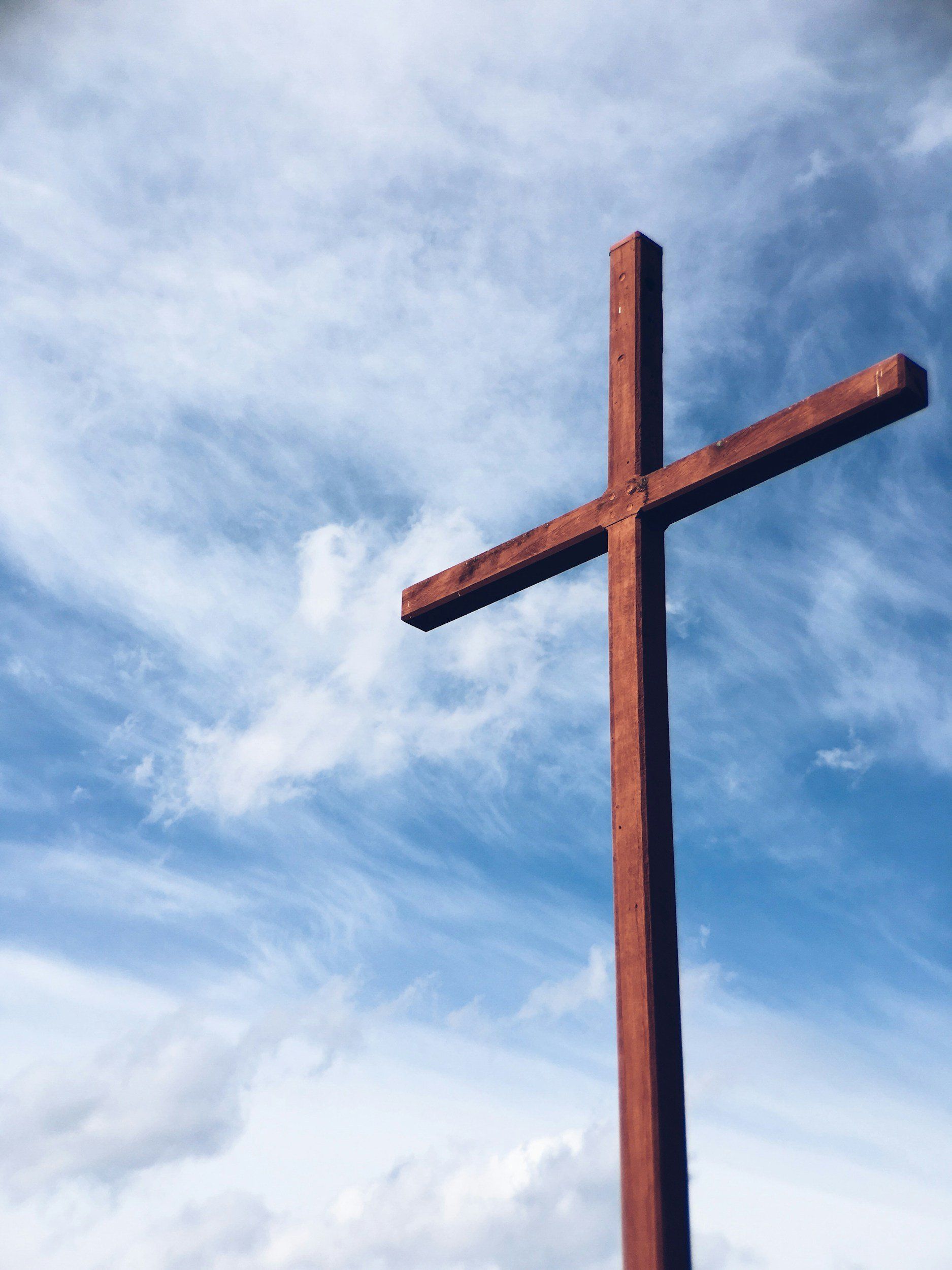 Rust-colored cross against a blue sky with wispy clouds
