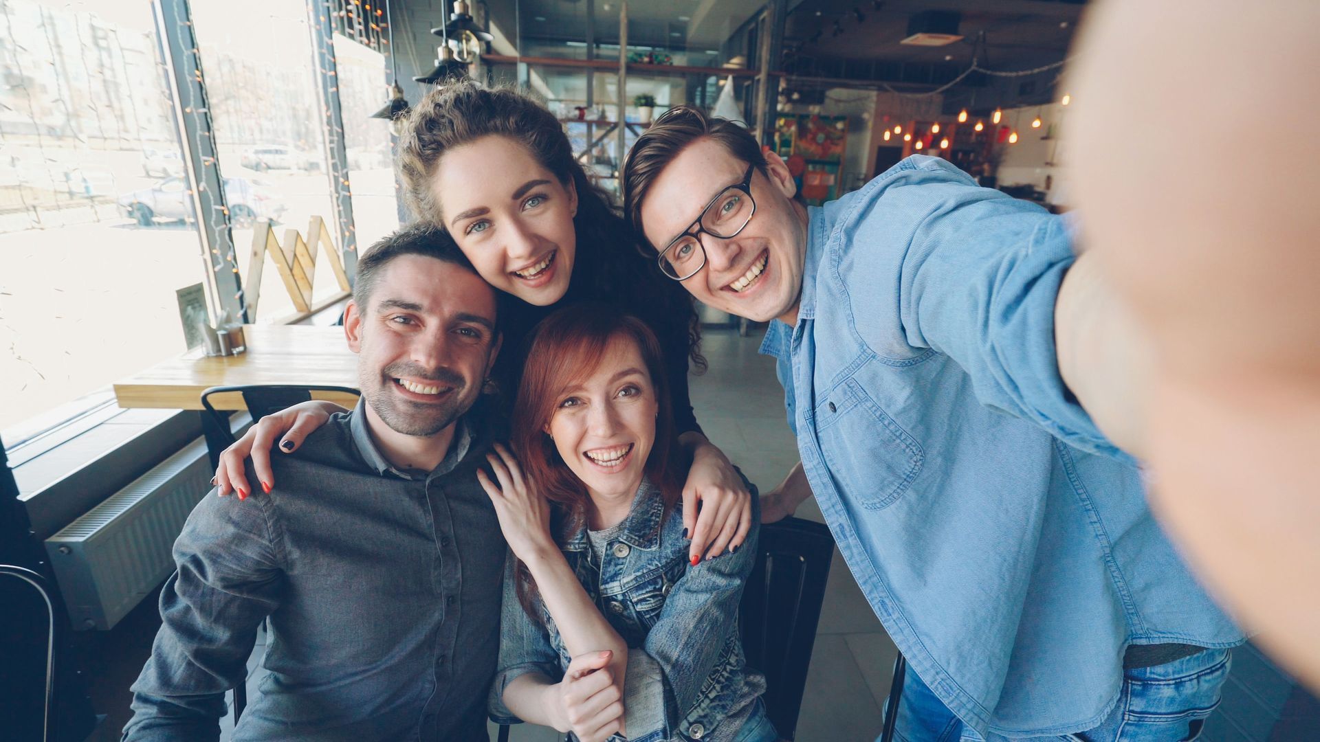 Four friends smiling and posing for a selfie in a cozy café.
