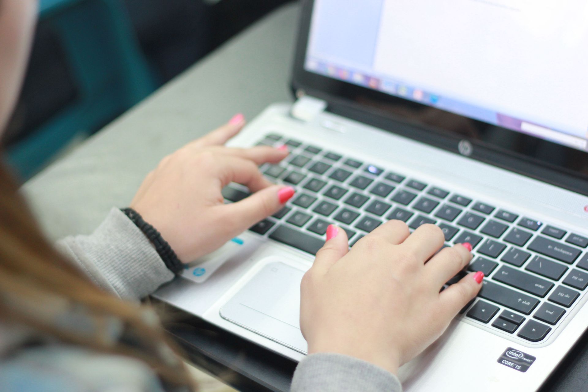 Hands typing on a laptop keyboard beside a bright screen