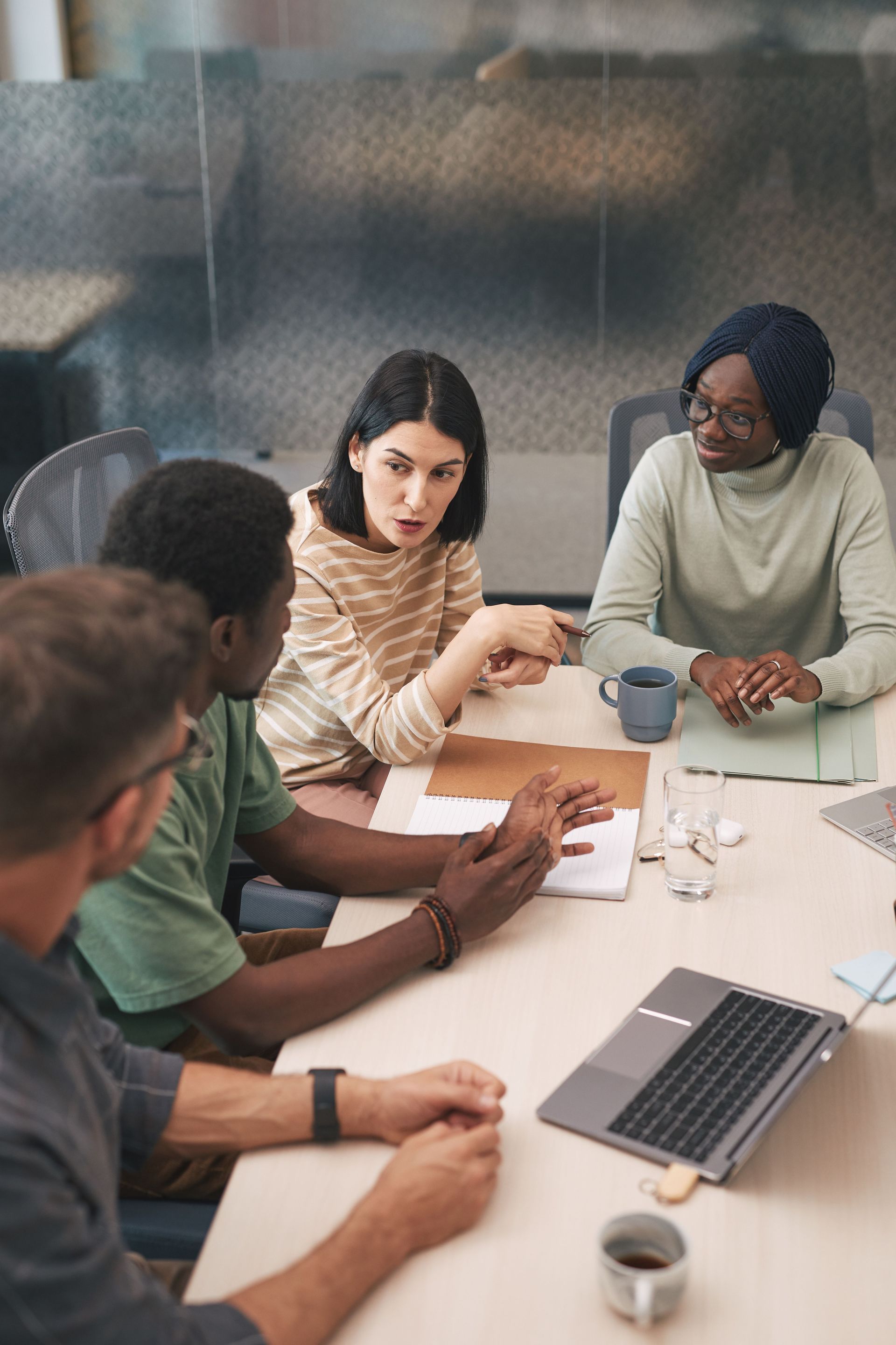 Team meeting around a table with laptop, coffee cups, and papers in a bright office