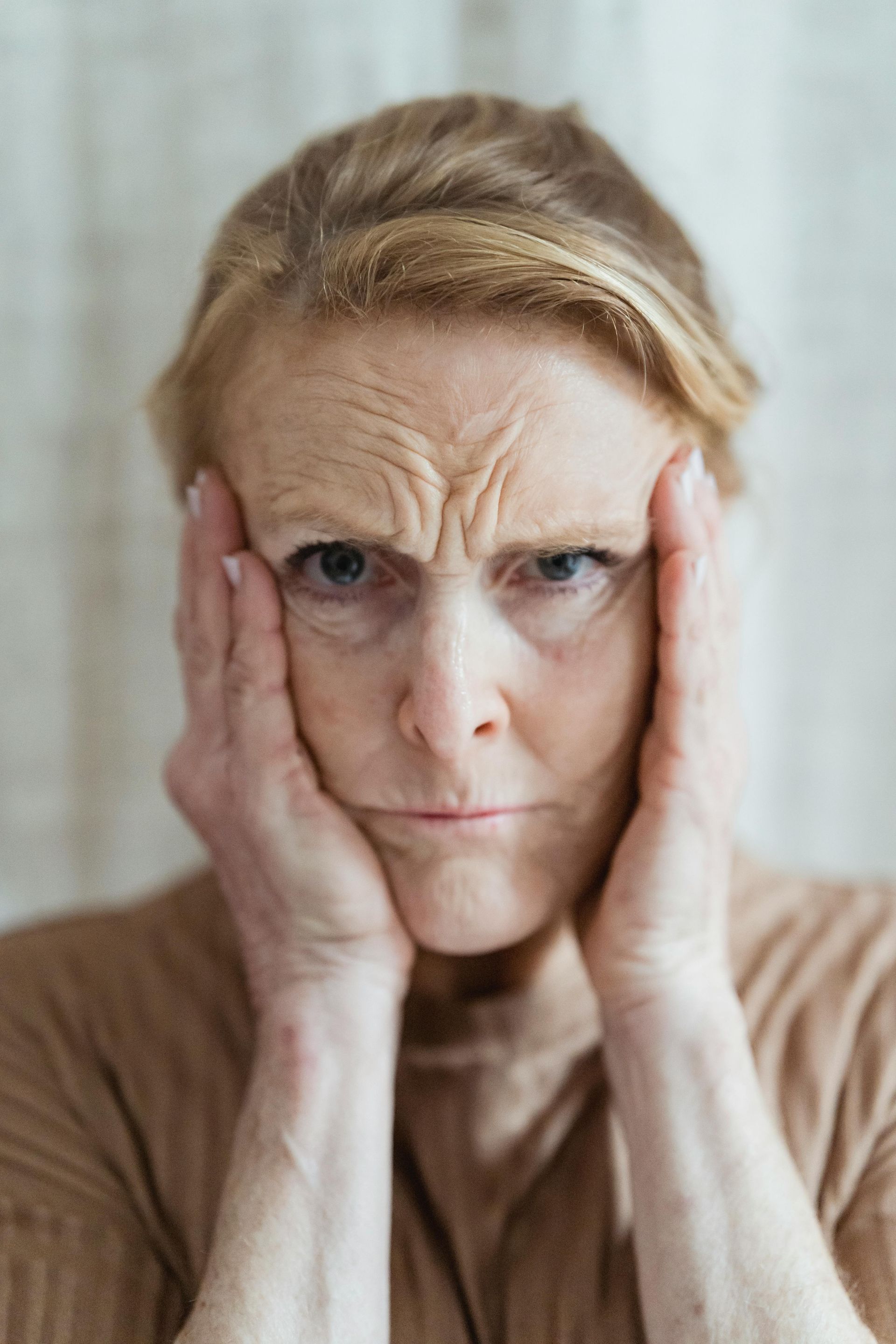 Person holding their face with both hands, looking stressed against a soft indoor background.