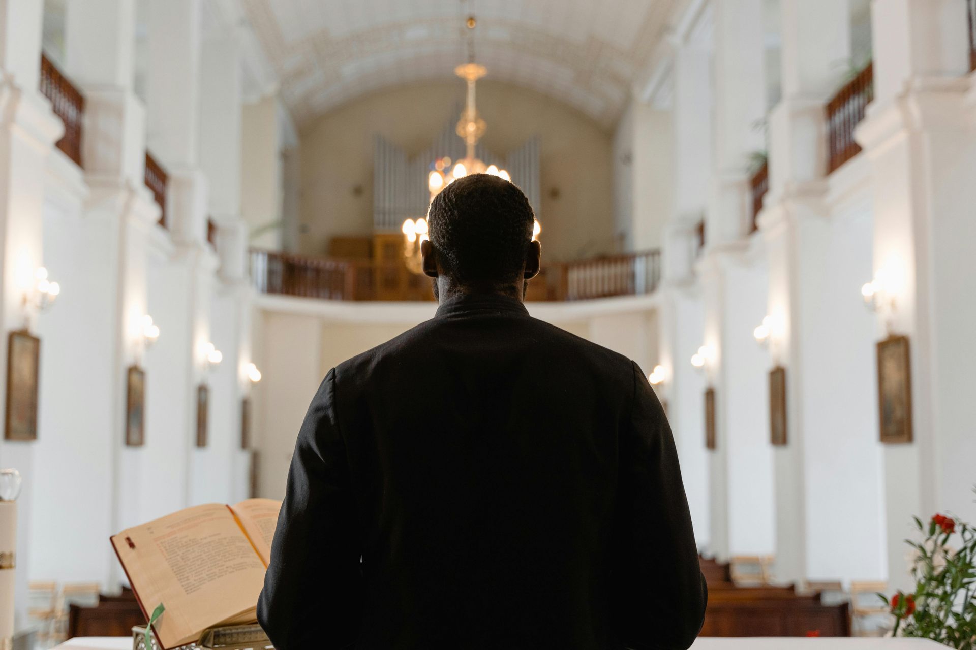 Person standing in a church aisle facing the altar, with an open book in the foreground.