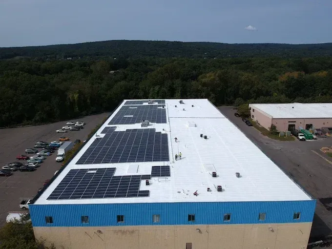 Aerial view of a large warehouse with solar panels on the roof and a parking lot beside it