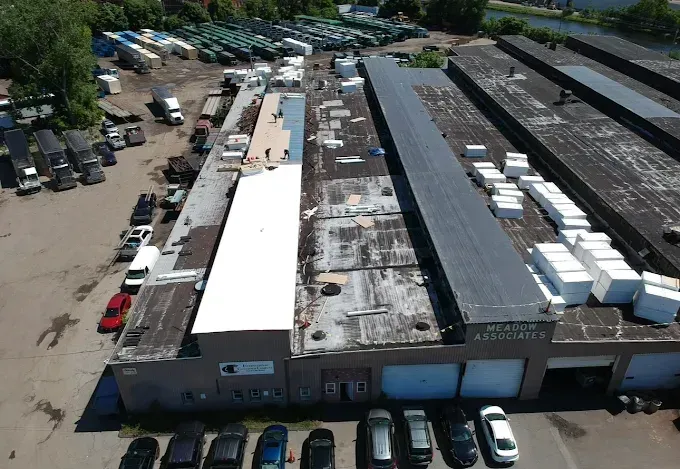 Aerial view of an industrial warehouse complex with parked cars and rows of rooftop equipment.