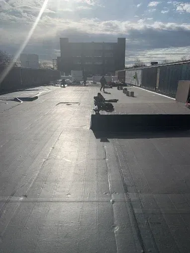 Rooftop with solar panels and a large building in the distance under a bright, cloudy sky