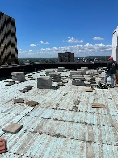 Rooftop with scattered concrete blocks under a bright blue sky; worker stands at right.