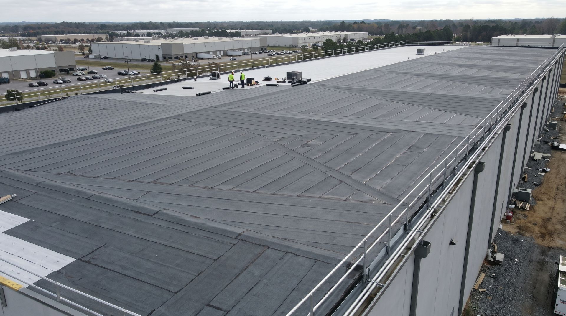 Aerial view of a large gray industrial warehouse roof with parking lots and roads in the background