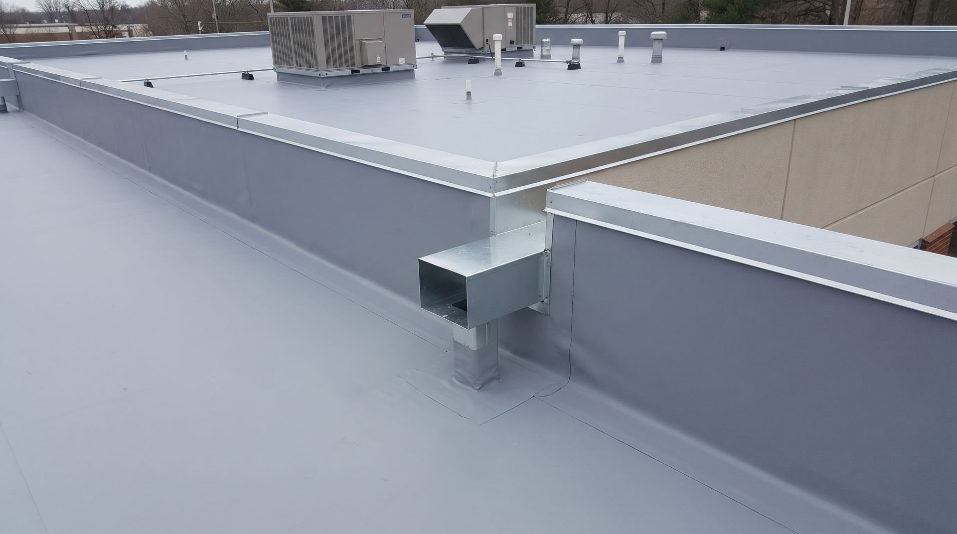 Rooftop with gray waterproof membrane, metal parapet, and HVAC units under an overcast sky