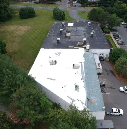 Aerial view of a flat-roofed white and gray building beside trees and a parking lot.