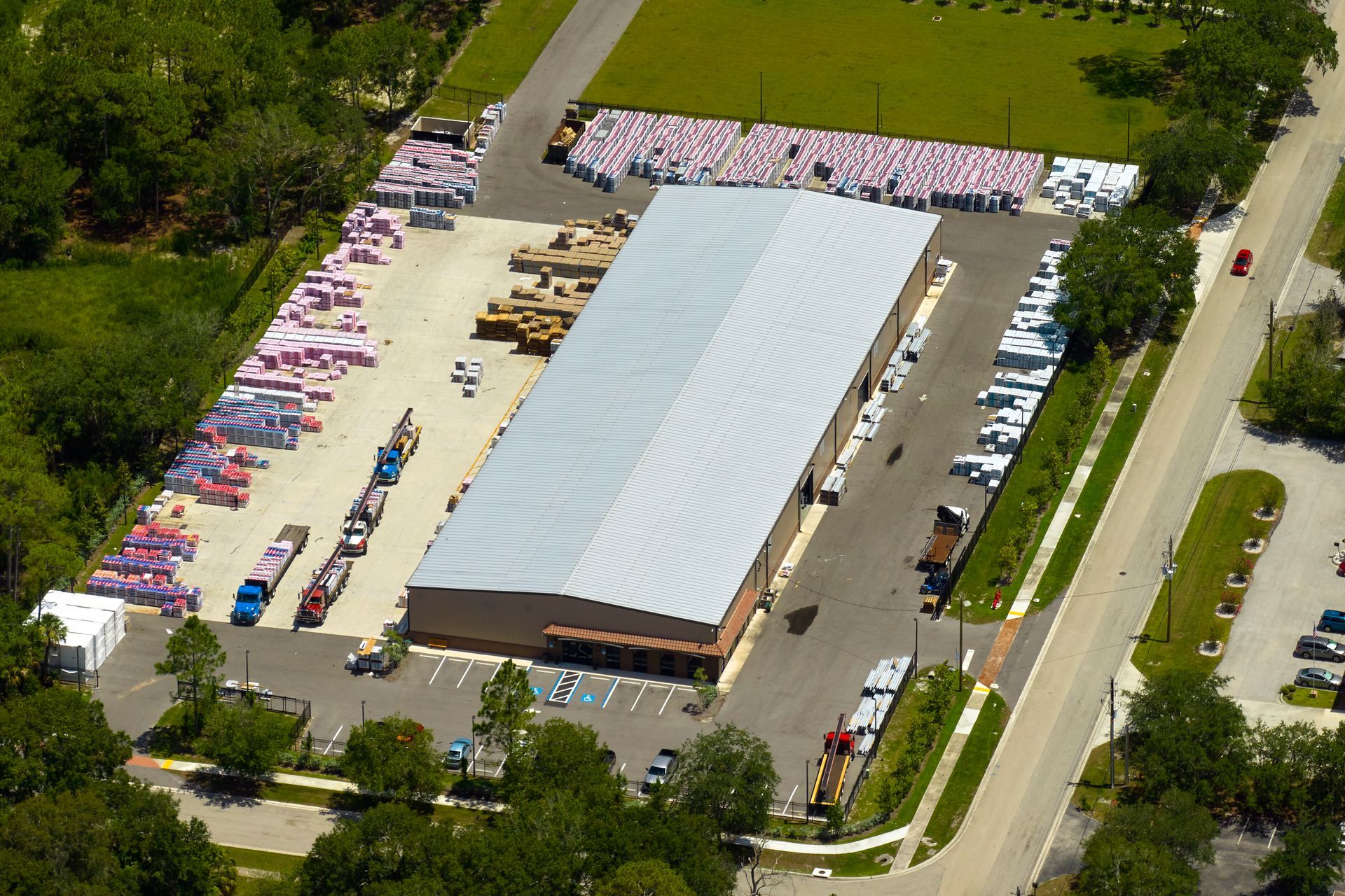 Aerial view of a large white-roofed building with rows of parked cars and trees around it