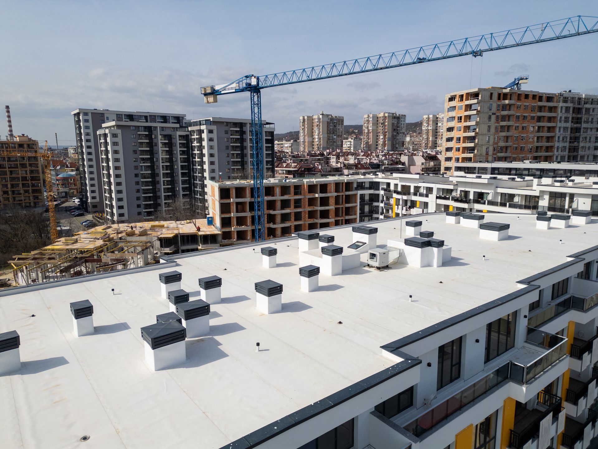 Rooftop view of a new apartment complex under construction with a crane and surrounding buildings