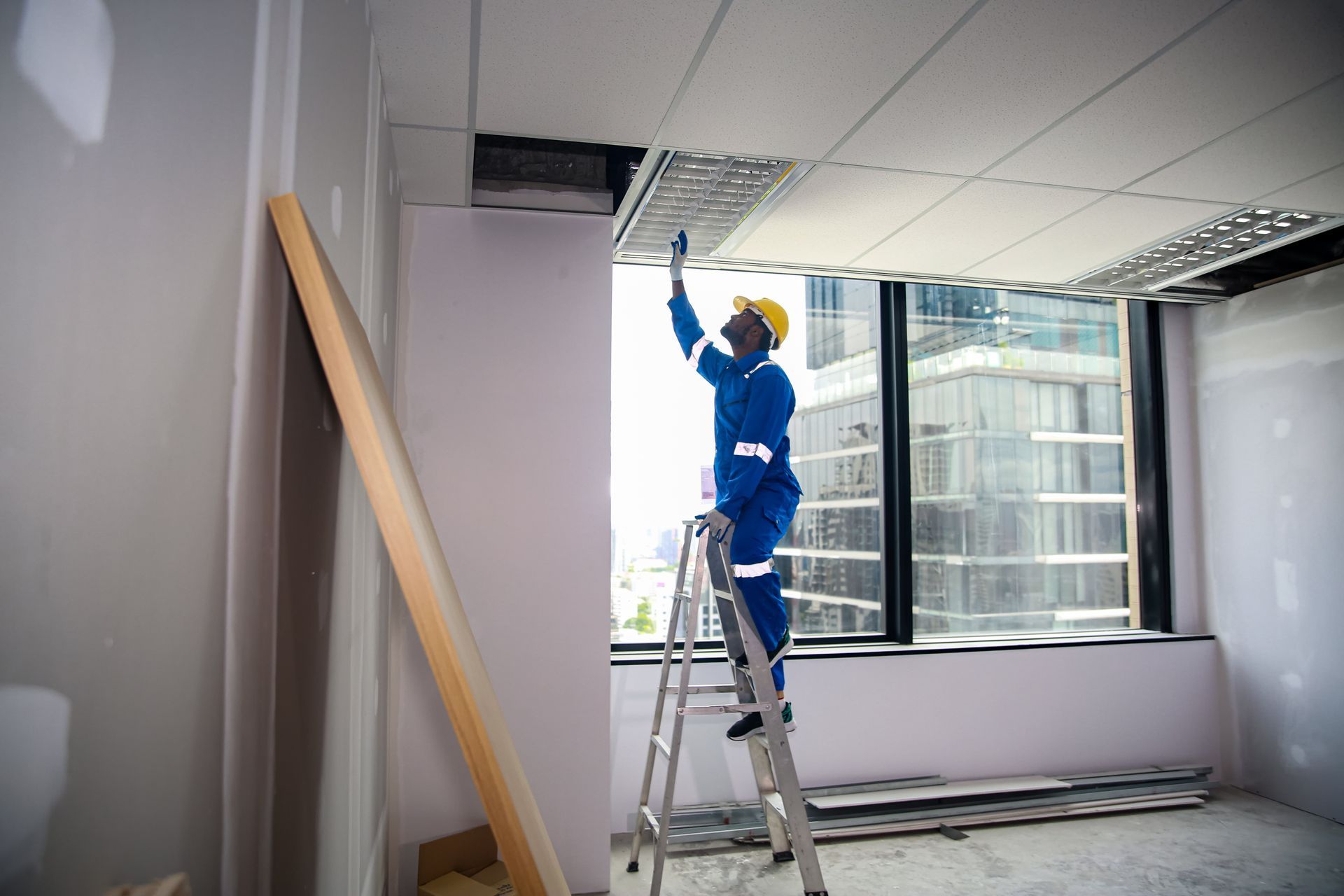 Worker on ladder installing ceiling panels in an office room