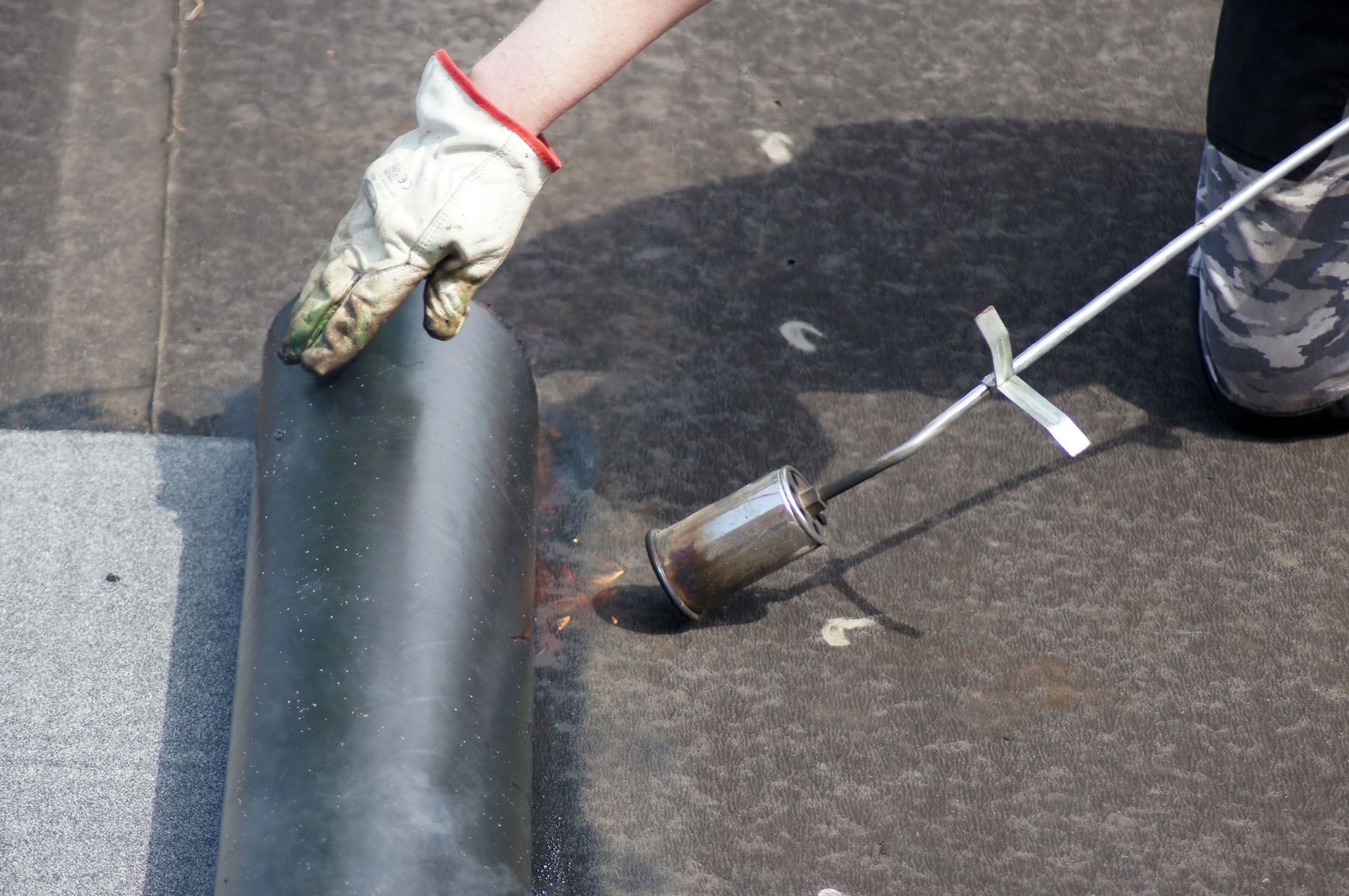 Worker heating roofing material with a torch on a flat roof