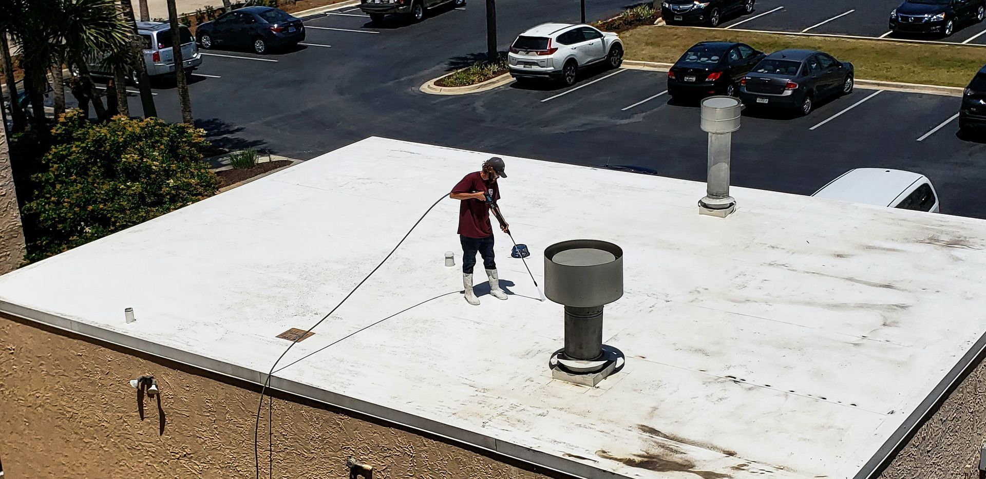 Person on a white rooftop using a long pole near parked cars below.
