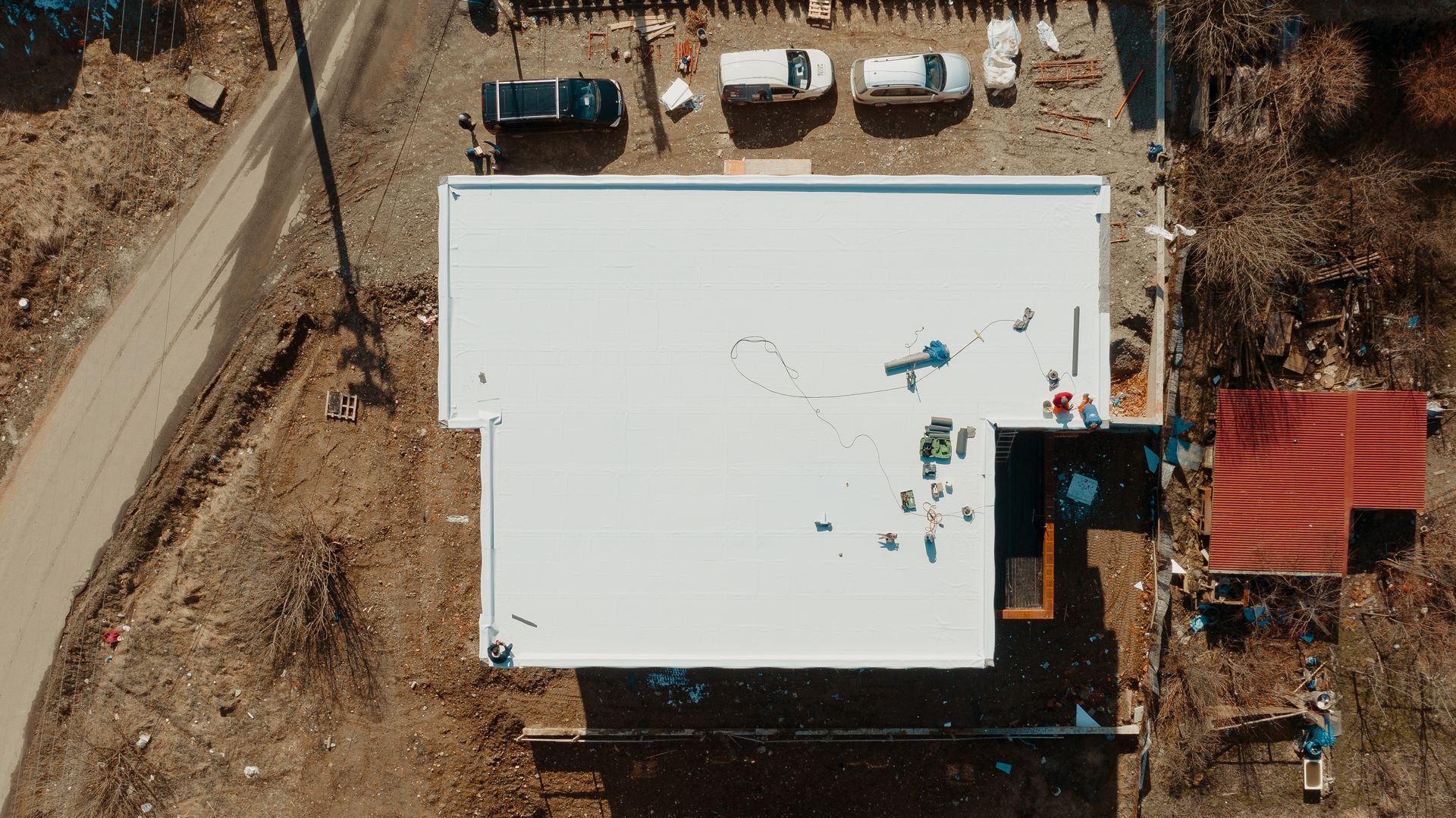 Worker in red cap applying white coating to a flat rooftop with a roller.
