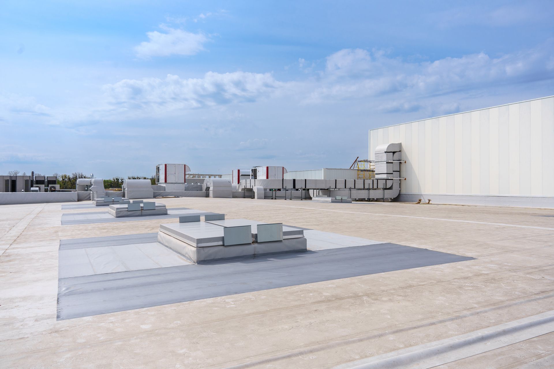 Rooftop with HVAC units and large white industrial building under a partly cloudy sky