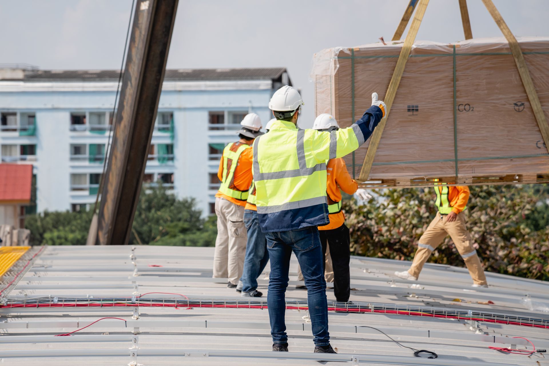 Construction workers in safety vests and hard hats lifting a large panel on a rooftop.