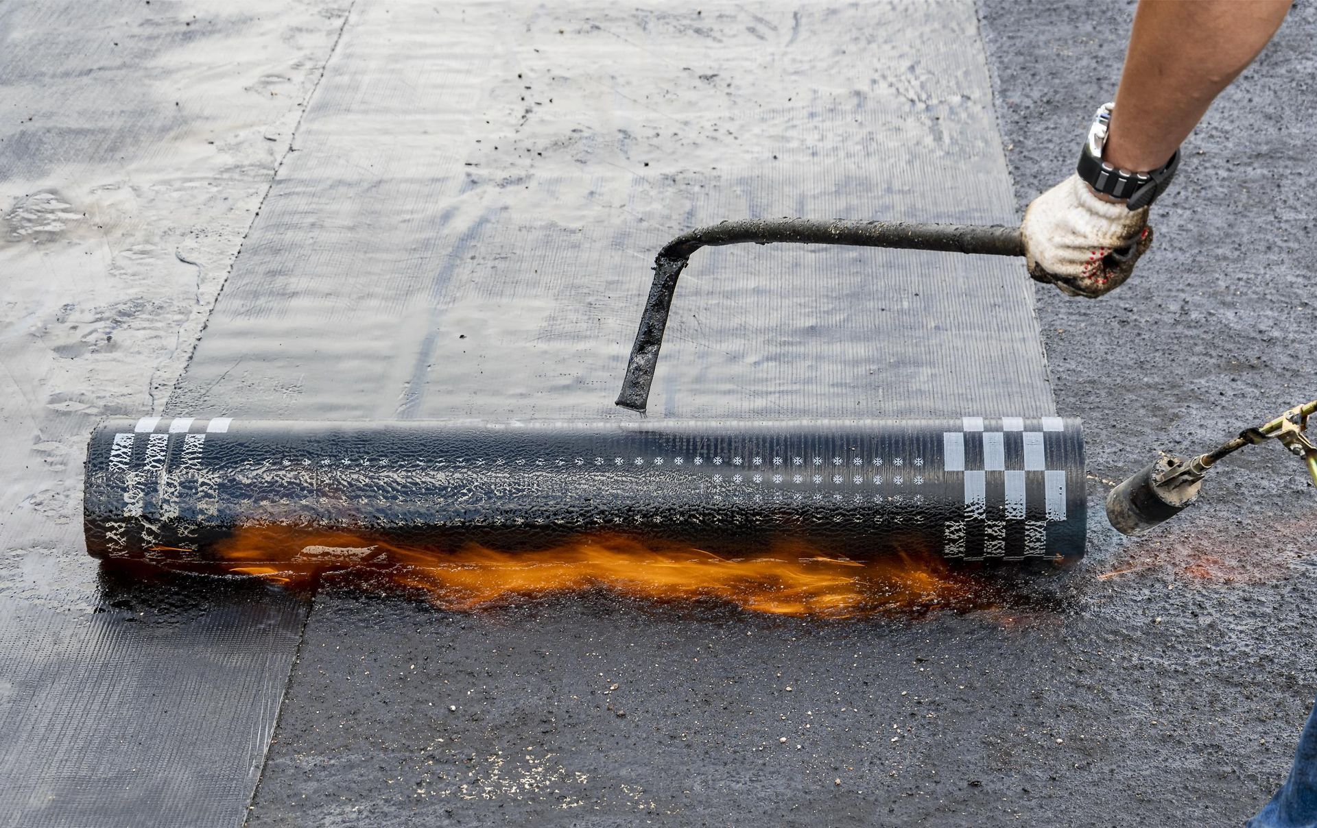 Worker rolling molten asphalt with a roller on a road surface