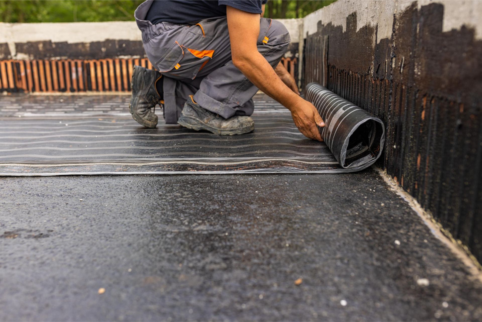 Worker rolling black waterproof membrane on a flat roof during installation