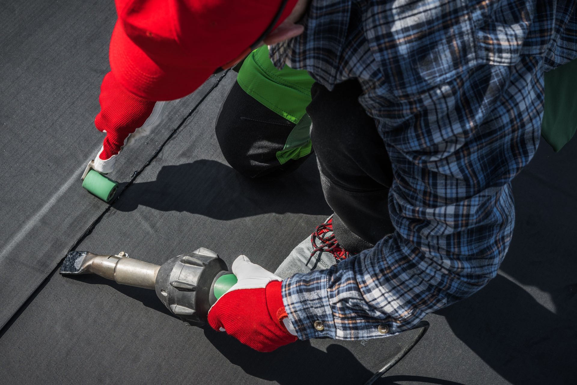 Worker using a heat gun to seal black roofing material on a roof