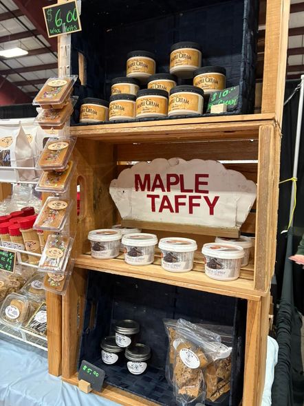 Wooden display stand with various jars and packages of maple taffy at a market.