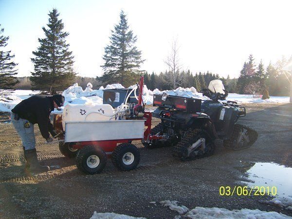 Man loading a small cart, attached to an ATV with snow tracks, on a snowy day.