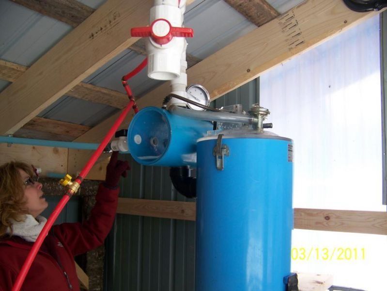 Person adjusts a red hose connected to a blue water tank with a PVC pipe and valve in a shed.